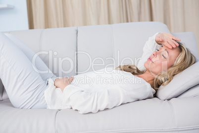Blonde lying on couch getting stomach and head ache