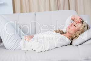 Blonde lying on couch getting stomach and head ache