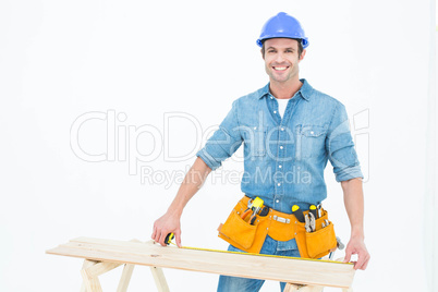 Happy male carpenter measuring wooden plank