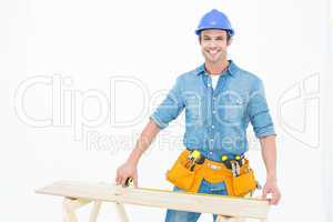 Happy male carpenter measuring wooden plank