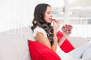 Pretty brunette eating strawberries on couch