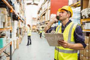 Warehouse worker talking on the phone holding clipboard