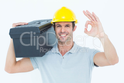Worker carrying tool box on shoulder while gesturing OK sign