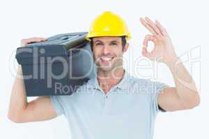 Worker carrying tool box on shoulder while gesturing OK sign