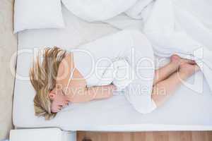 Blonde woman lying in bed getting stomach pain