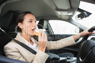 Pretty businesswoman having doughnut while driving