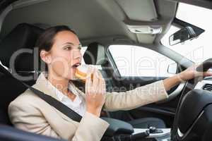 Pretty businesswoman having doughnut while driving