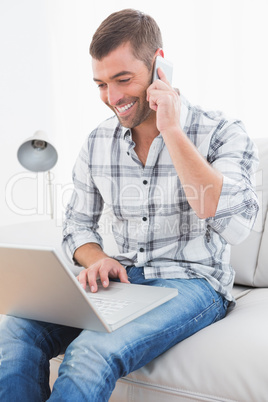 Smiling man on a phone with a laptop at home Smiling man on a phone with a laptop at home