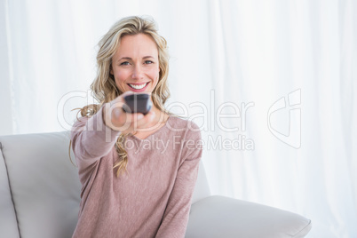 Happy blonde on couch changing tv channel