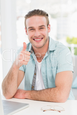 Positive businessman at desk with thumb up