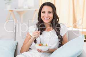 Pretty brunette eating salad on couch