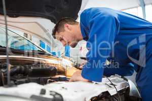 Mechanic examining under hood of car with torch