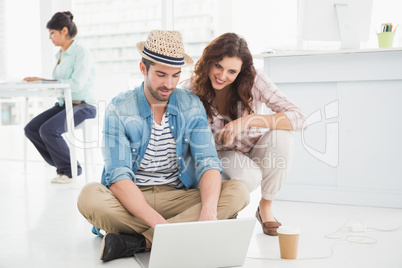 Smiling colleagues sitting on the floor using laptop