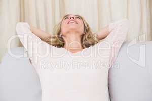 Happy blonde relaxing with hands behind head on couch