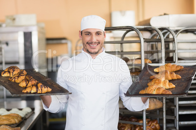 Smiling baker holding trays of croissants