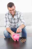 Smiling man putting coins in a piggy bank