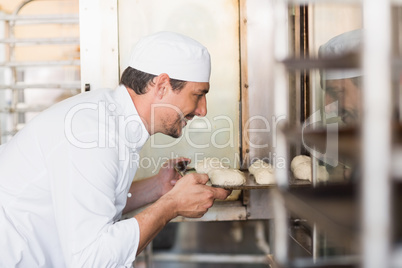 Smiling baker putting dough in oven