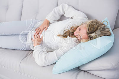 Blonde lying on couch getting stomach pain