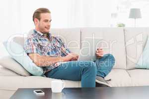 Relaxed man sitting on sofa using laptop