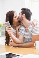 Young man using smartphone while girlfriend kisses him