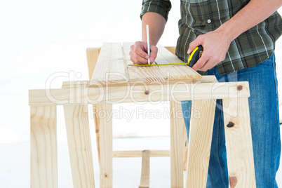 Worker using measure tape to mark on wooden plank