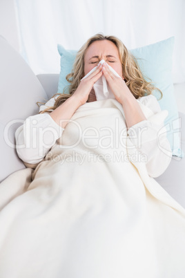 Blonde lying on couch sneezing on tissue