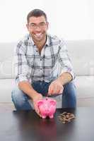 A smiling man putting coins in a piggy bank