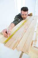 Worker using measure tape to mark on wooden plank
