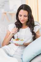 Pretty brunette eating salad on couch