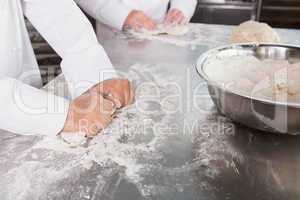 Close up of bakers kneading dough at counter