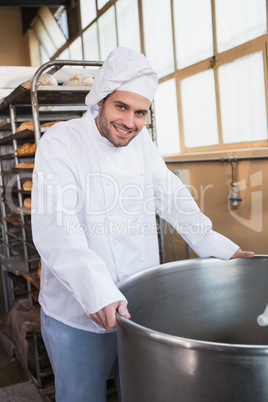Smiling baker leaning on industrial mixer