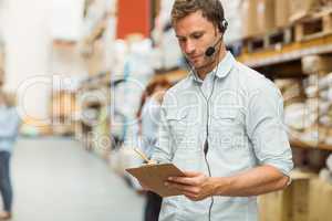 Warehouse manager wearing headset writing on clipboard