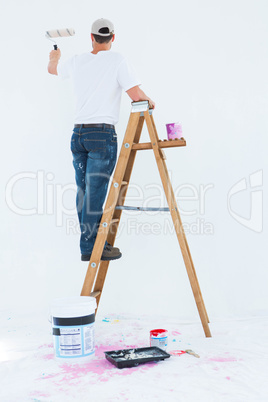 Man on ladder painting with roller