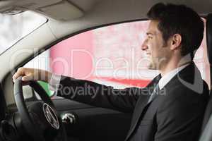 Smiling businessman at the wheel sitting in a car for sale