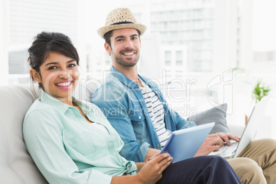 Smiling coworkers using tablet and laptop on couch Smiling coworkers using tablet and laptop on couch