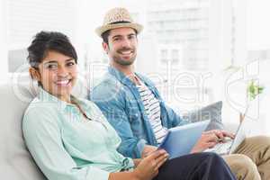 Smiling coworkers using tablet and laptop on couch