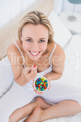 Happy blonde eating sweets in bed