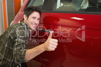 Smiling man hugging a red car while giving thumbs up