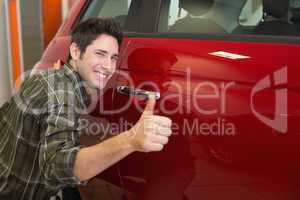 Smiling man hugging a red car while giving thumbs up