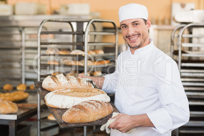 Smiling baker holding tray of bread