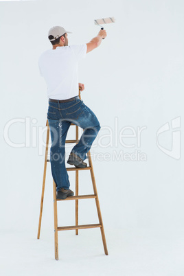 Man on ladder painting with roller