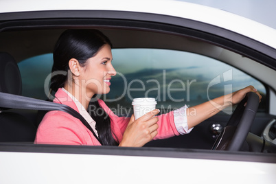 Smiling woman driving car while drinking coffee