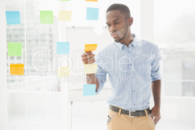 Casual businessman reading sticky notes on window