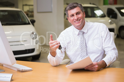 Smiling salesman holding car key and a document