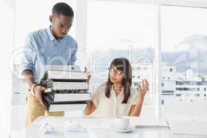 Man giving pile of files to his exasperated colleague