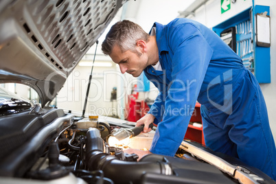 Mechanic examining under hood of car with torch