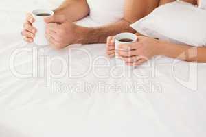 Mid section of young couple having coffee in bed
