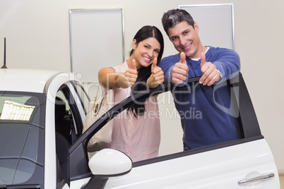 Smiling couple standing while giving thumbs up