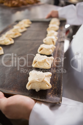 Close up of baker holding tray of raw dough
