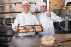 Team of bakers smiling at camera with trays of croissants